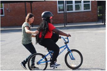 adult teaches a fifth-grade student at Washington STEM Elementary School to ride a bicycle so she can participate in the bike skills drills the next day