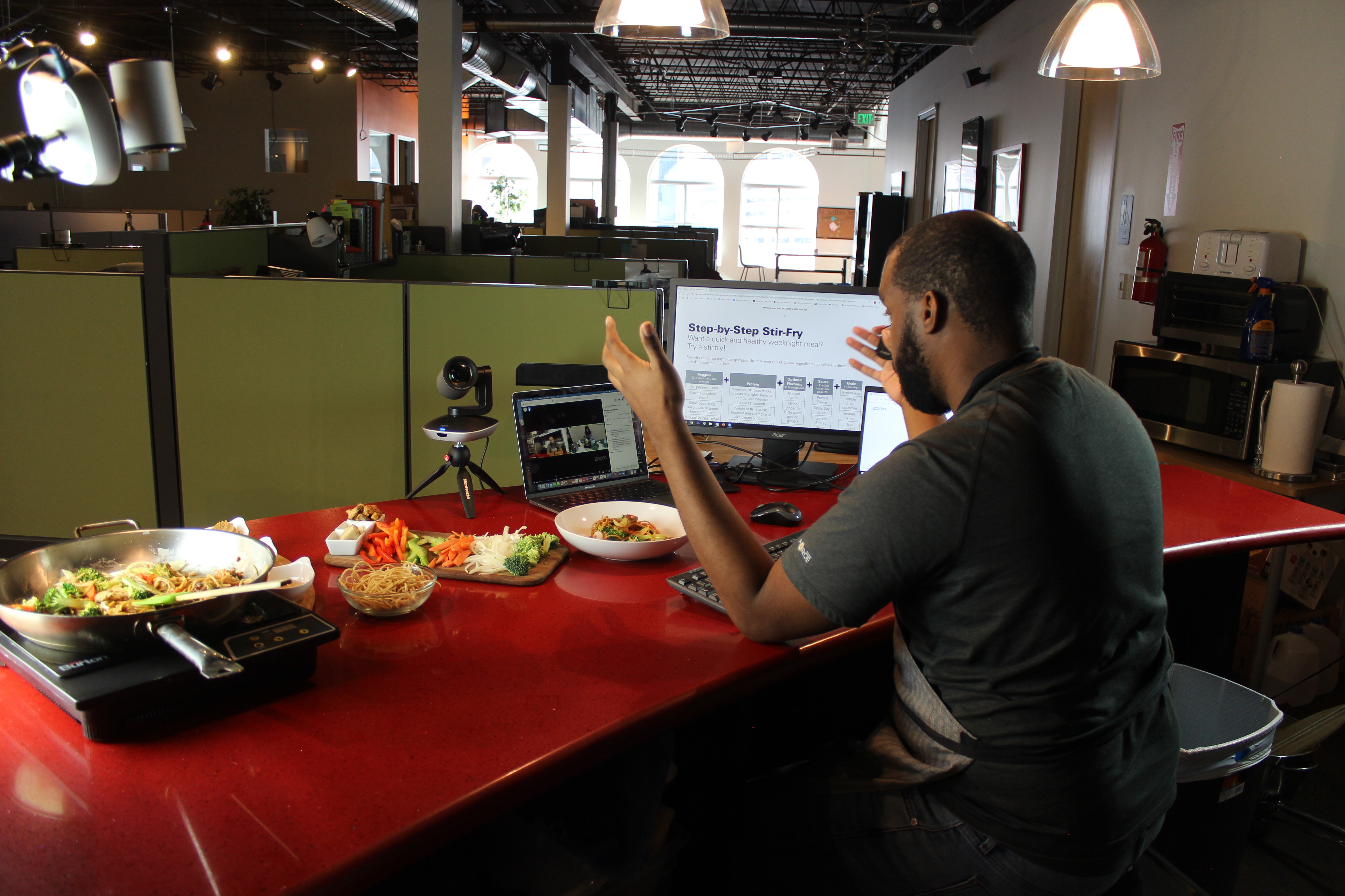 an instructor gives an online cooking demonstration with a skillet of food and chopped veggies