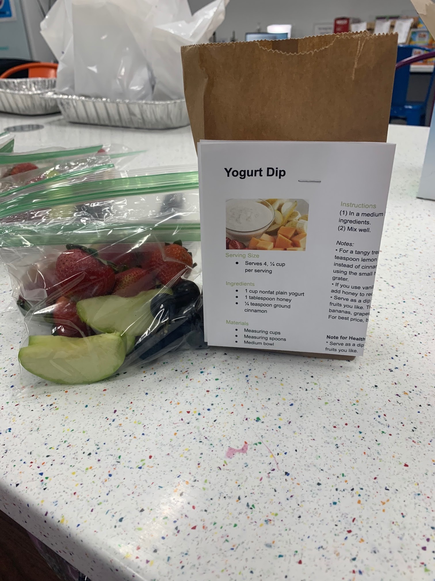 creating activity kits for pickup by camp participants: fruit and veggies in a plastic bag with a recipe attached
