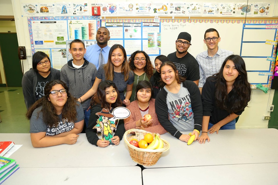 a bunch of teens standing behind baskets of fruit