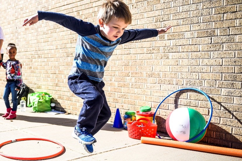 A preschooler jumping and playing with a hulahoop.