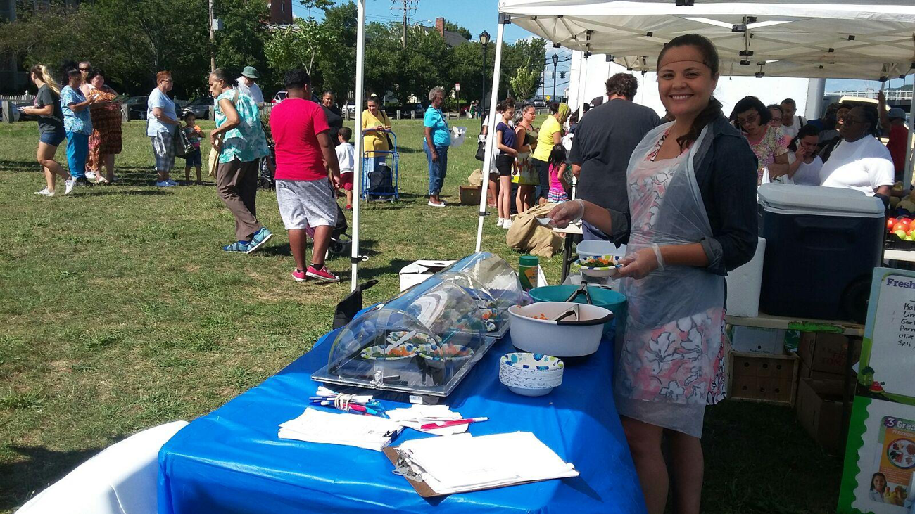 educator stands at a food tasting table giving out samples