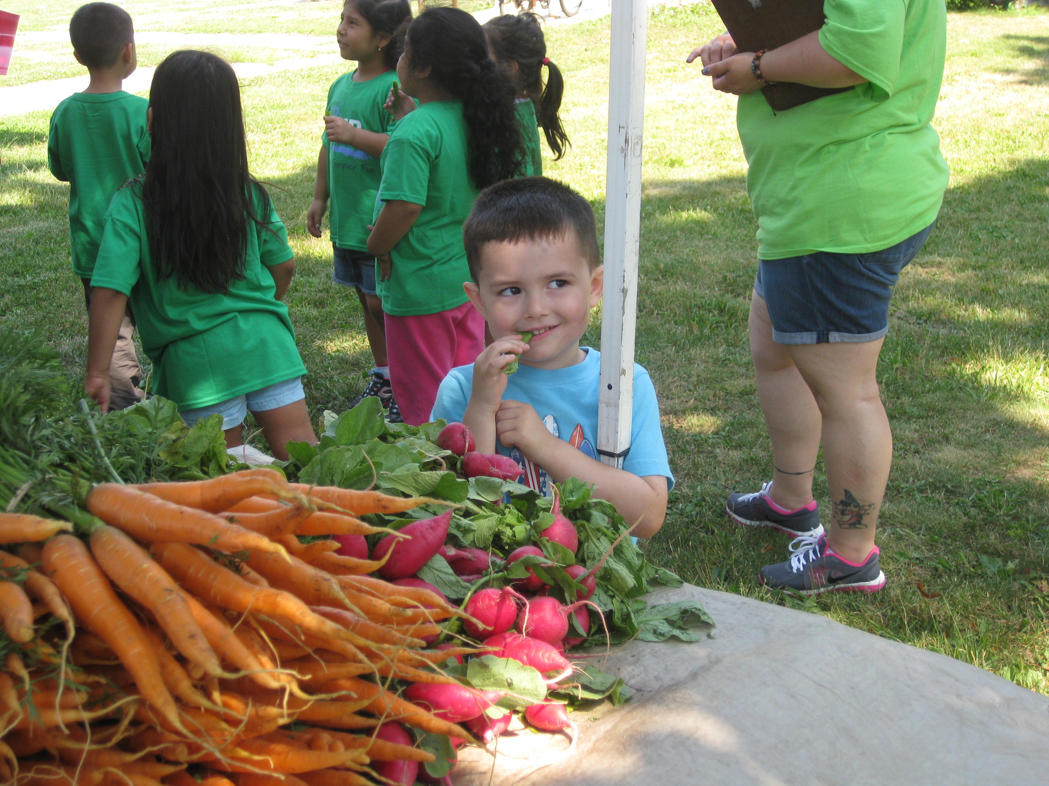 small boy eating a snap pea at a farmers market