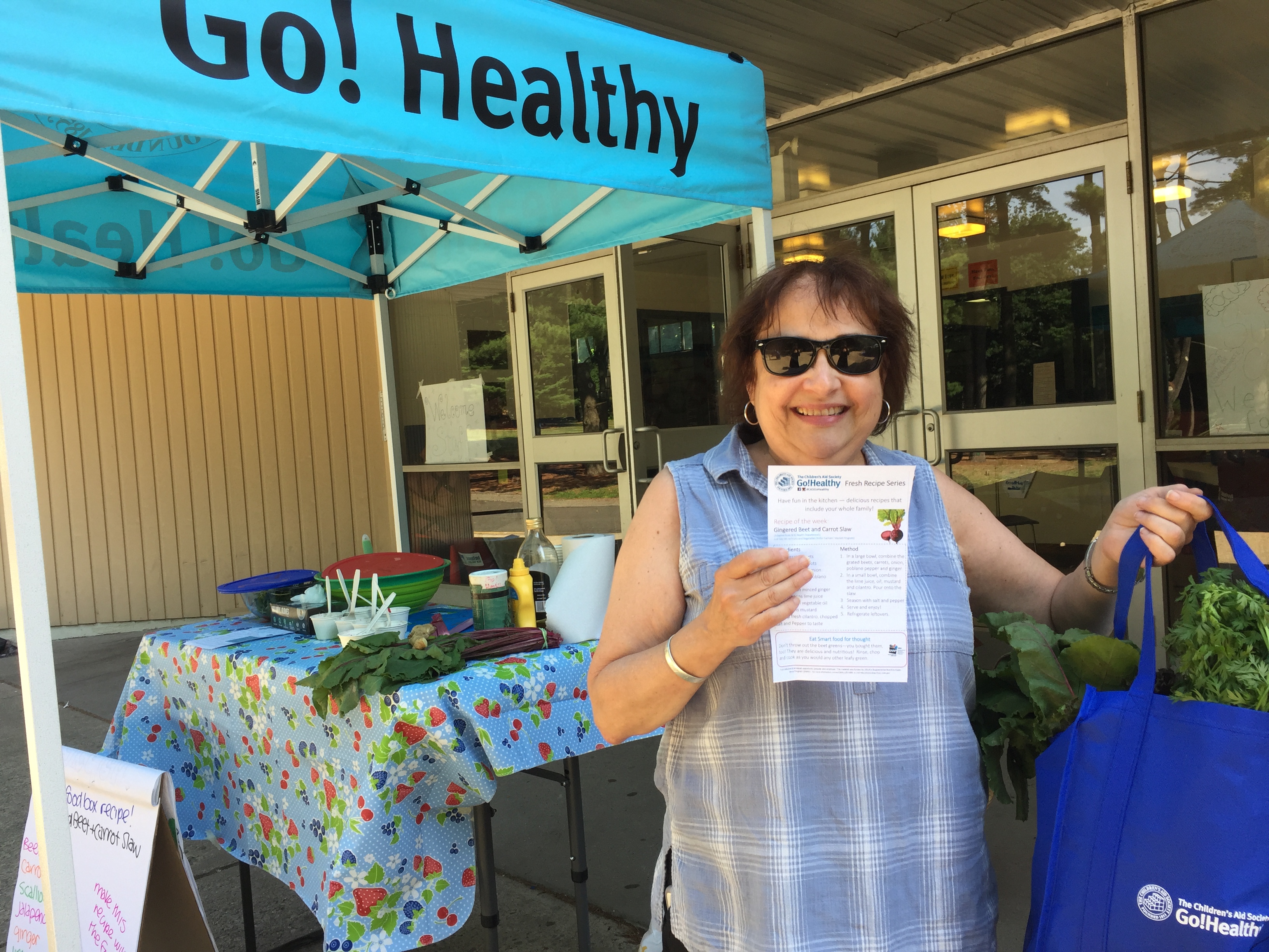 smiling woman with a nutrition education sheet and a bag of produce