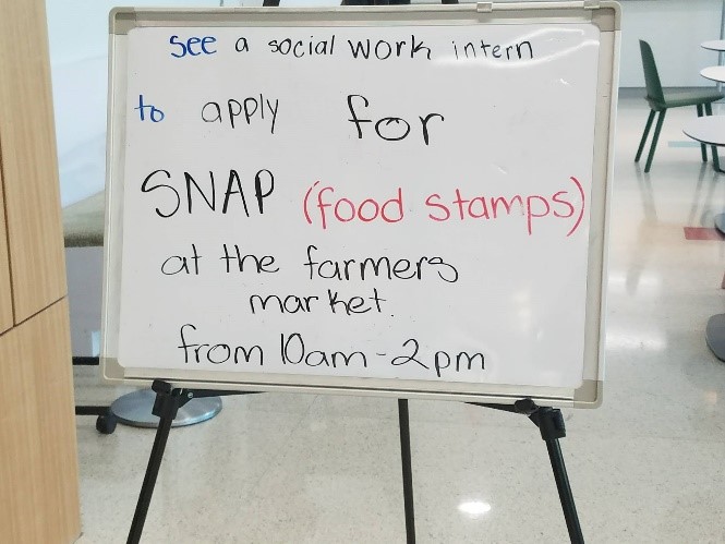 White board with text "See a socail work intern to apply for SNAP (Food Stamps) at the farmers market from 10am - 2pm"