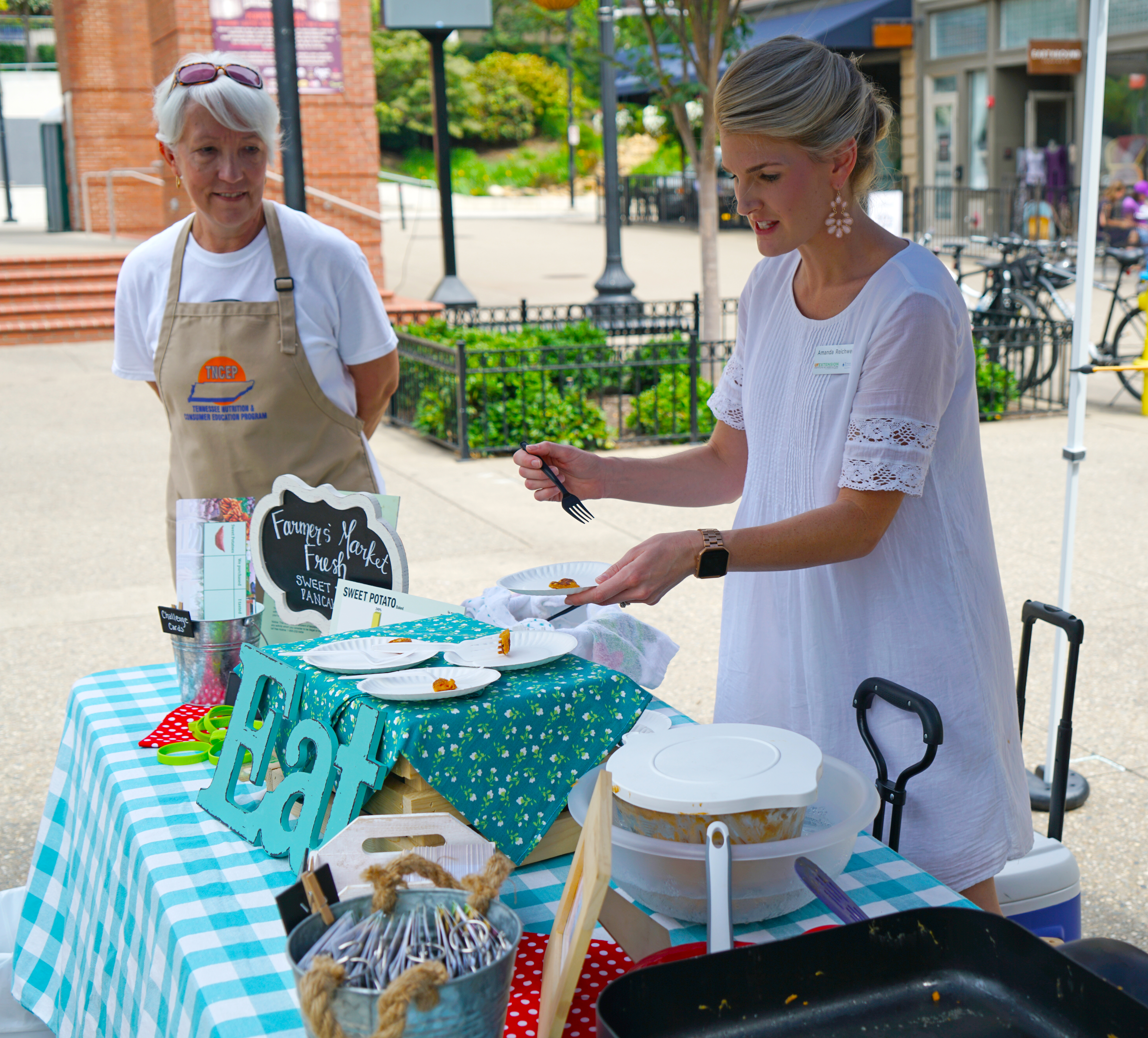 two women serve food samples at a Farmers Market