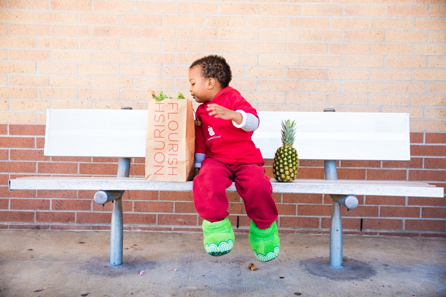 a boy sits on a bench with a bag of groceries