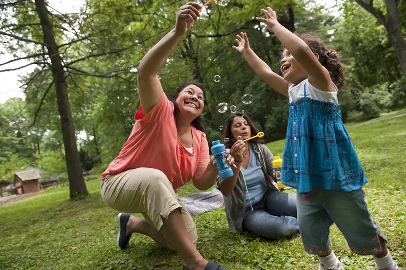 2 women blowing bubbles with a preschool aged girl.