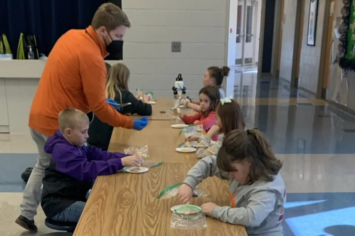an adult provides kids with snacks while sitting at a table