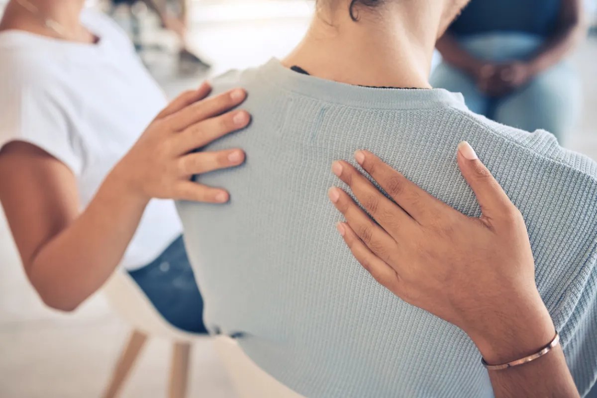 close up of a woman sitting in a group with supporting hands on her back