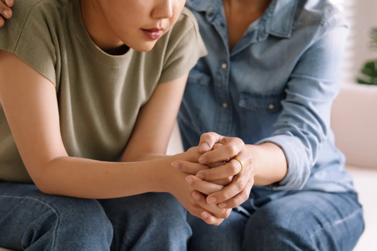 2 people sitting on a couch holding hands suportively
