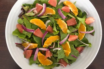 oranges, red onions, and greens in a white bowl