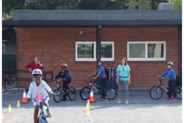 Smiling fifth-grade student at Washington STEM Elementary School riding a bicycle practicing the bike skills drills, while her classmates wait their turn to execute the course. 