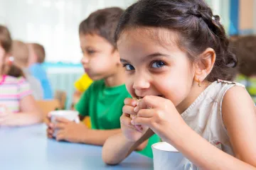 A preschool girl taking a bite of her lunch