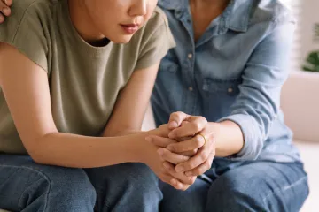 2 people sitting on a couch holding hands suportively