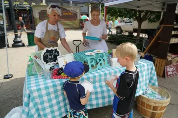 two boys try food from a sample table at a Farmers Market