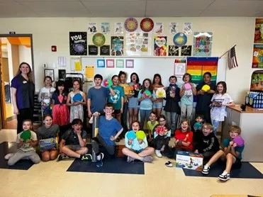 5th grade class of students in their classroom posed for a group photo holding items from their rainy day recess kit like foam dice, and activity shapes.