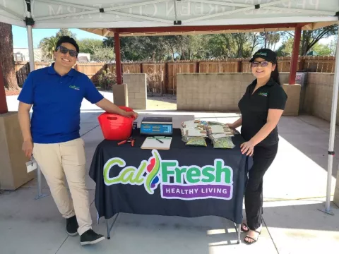 Two people stand next to a table with the CalFresh logo